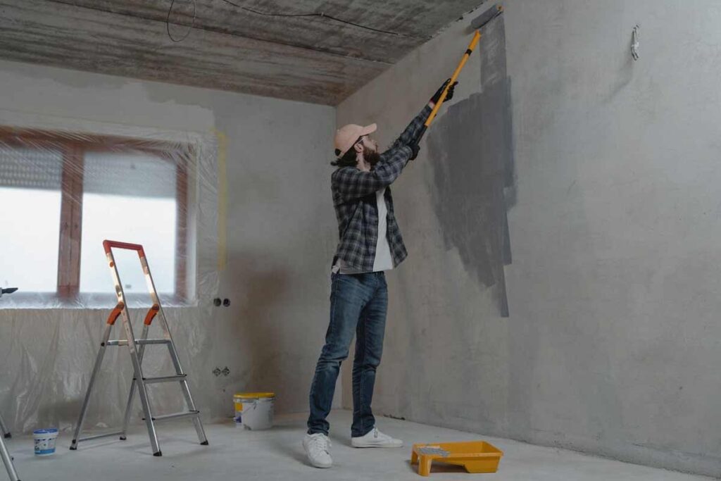 A professional painter in Wichita, KS, applying primer to a home’s interior wall, ensuring a smooth and even base for high-quality paint application. The workspace is neatly prepped with floor coverings and painter’s tape.