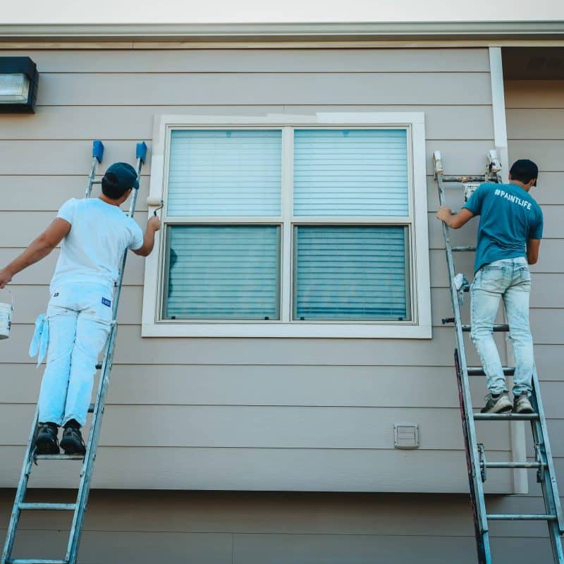 Two painters update a home exterior with a trending neutral paint color, reflecting the latest exterior paint trends for modern homes.