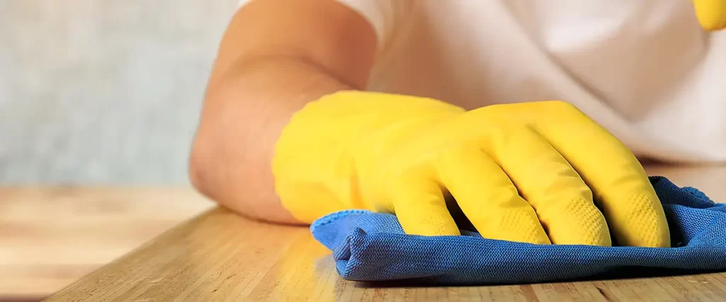 a professional contractor wearing yellow gloves cleans wooden surface with precision
