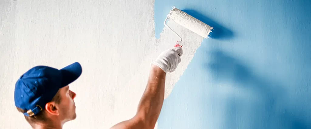 professional house painter in a blue cap expertly applies white paint to a blue wall using a roller brush