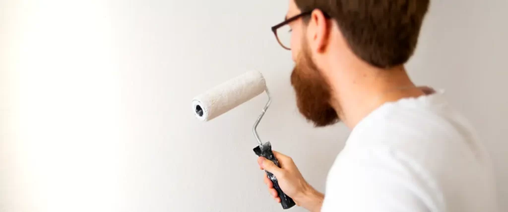 applying white paint with a roller on a wall