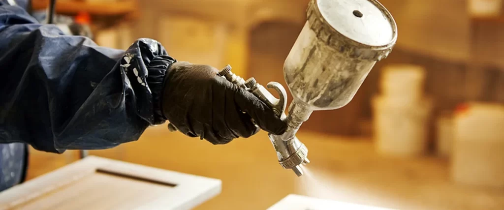 professional contractor using commercial grade paint sprayer on wooden cabinet door