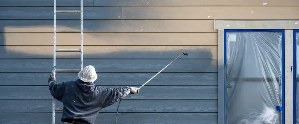 Exterior painter spraying dark blue paint on house siding