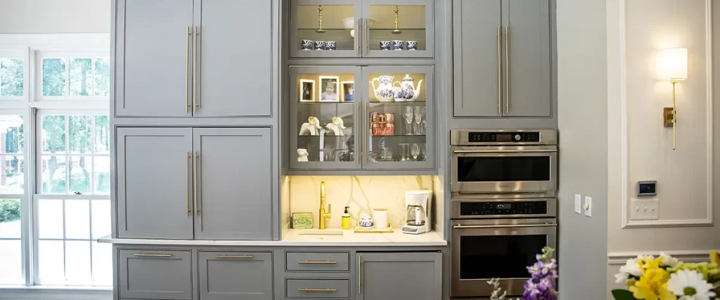 Gray painted kitchen cabinets with glass display and gold handles