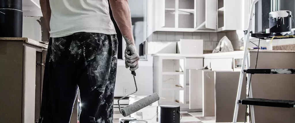 Painter using roller to apply white paint on kitchen cabinets