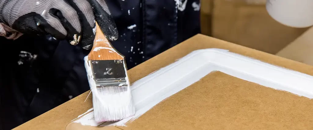 Professional painter applying white paint to a cabinet door with brush